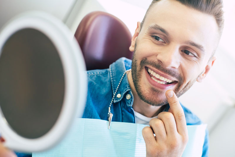 a patient smiling and pointing at his teeth in a mirror after he has gotten a crown lengthening procedure.