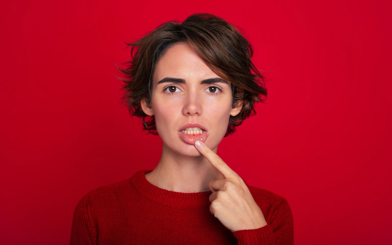 Close-up portrait of gum inflammation. A cropped shot of a young woman showing red bleeding gums isolated on a bright red background. Dentistry, dental care
